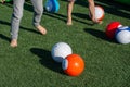 Vibrant billiards soccer/footballs balls on the green grass with children`s feet kicking for recreation and fun outdoors Royalty Free Stock Photo