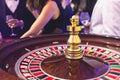 Vibrant casino table with roulette in motion, with casino chips, tokens, the hand of croupier, dollar bill money and a group of Royalty Free Stock Photo