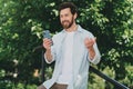 Young man cheerfully interacting with his smartphone outdoors surrounded by lush greenery on a sunny day in the city Royalty Free Stock Photo