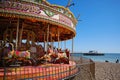 Brightly coloured carousel, with Worthing pier, stretching out to sea. West Sussex, England.