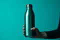 Vibrant cyan backdrop emphasizes female hand clutching steel water bottle
