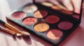 Vibrant eyeshadow palette featuring warm and shimmering shades with assorted makeup brushes on a soft pink surface for creative Royalty Free Stock Photo