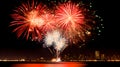 fireworks burst, city skyline silhouette, fiery red radiance, white starbursts, night celebration, reflective water, urban