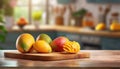 A selection of fresh fruit: mango, sitting on a chopping board against blurred kitchen background copy space