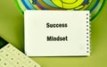 On a vibrant green surface, a notepad displays the words success mindset alongside a calculator and colorful background. This Royalty Free Stock Photo