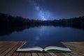 Vibrant Milky Way composite image over landscape of still lake coming out of pages in magical story book