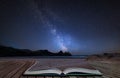 Vibrant Milky Way composite image over landscape of yellow sandy beach Three Cliffs bay coming out of pages in magical story book