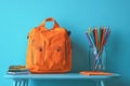 Vibrant Orange Backpack, Stack of Notebooks, Color Pencils in Jar on Blue Tabletop Royalty Free Stock Photo