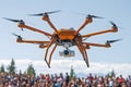 Orange multirotor drone with camera flying over crowd outdoors Royalty Free Stock Photo