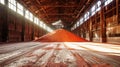 A vibrant pile of red sand stands out in a sprawling warehouse filled with potash fertilizers. The sand glows like embers in the