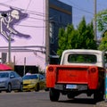 a large pink mural hangs above a city street with parked cars and an open top Royalty Free Stock Photo