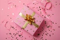 A vibrant pink present adorned with a gold bow surrounded by golden confetti Royalty Free Stock Photo