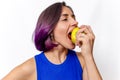 Cheerful woman eating green apple isolated on white background. Blue dress, purple hair. Side view Royalty Free Stock Photo