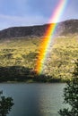 Vibrant rainbow descending onto a serene lake in Oppdal, Norway, with rustic mountain huts