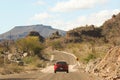 a red car traveling down a dirt road past mountains and desert