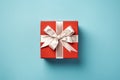 Vibrant red gift box decorated with white satin ribbon and bow, against a pastel blue backdrop Royalty Free Stock Photo