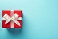 Vibrant red gift box decorated with white satin ribbon and bow, against a pastel blue backdrop Royalty Free Stock Photo