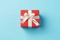 Vibrant red gift box decorated with white satin ribbon and bow, against a pastel blue backdrop Royalty Free Stock Photo