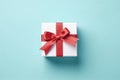 Vibrant red gift box decorated with white satin ribbon and bow, against a pastel blue backdrop Royalty Free Stock Photo