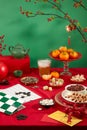 On a vibrant red and green backdrop, a go chess board, a glass of soft drink, plates of tangerines, sunflower seeds, colorful