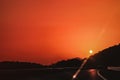 Vibrant red orange sunset sky over highway with one car and Sun over mountains silhouette Royalty Free Stock Photo