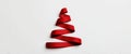 A vibrant red ribbon is skillfully arranged into the shape of a Christmas tree, resting on a clean white background. This Royalty Free Stock Photo