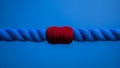 A vibrant red yarn tightly binds two thick blue rope strands, creating a striking contrast against a solid blue Royalty Free Stock Photo