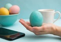 A hand holding a turquoise Easter egg with colorful eggs in a bowl Royalty Free Stock Photo