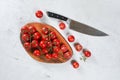 Vibrant small red tomatoes with green vines on wooden chopping board, large chef knife near, white stone table under, view from Royalty Free Stock Photo