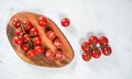 Vibrant small red tomatoes with green vines on wooden chopping board, white stone table under, view from above Royalty Free Stock Photo