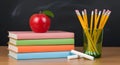 A vibrant stack of schoolbooks, a crisp red apple, sharp pencils, and classic chalk set against a chalkboard. Perfect for Royalty Free Stock Photo