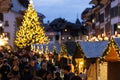 Vibrant street scene at night with people milling around decorated booths at Christmas.