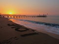 Vibrant sunset illuminated against the soft ocean, the word LOVE written in the sand