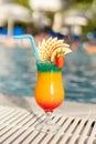 A vibrant tropical drink sits next to a sparkling pool under the sun Royalty Free Stock Photo