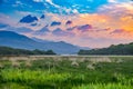 Vibrant and colorful mountain range sunset meadow landscape with green grass and orange clouds