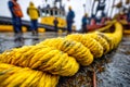 Close-up of a thick yellow maritime rope on a wet dock with workers and ships in the background Royalty Free Stock Photo