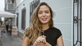 Vibrant, young and beautiful hispanic woman confidently expressing joy while speaking and smiling on an urban street, enchanting Royalty Free Stock Photo