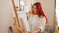 Vibrant young redhead artist, full of creativity, joyfully preparing to paint, standing in the midst of her art studio, ready to Royalty Free Stock Photo