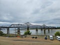 The Vicksburg Bridge over the flowing waters of the Mississippi river with a barge sailing underneath, lush green trees Royalty Free Stock Photo