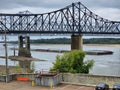 The Vicksburg Bridge over the flowing waters of the Mississippi river with a barge sailing underneath, lush green trees Royalty Free Stock Photo