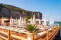 People resting on deckchairs under white parasols on wooden terrace in Vico Equensea coastal town near Naples with rocky mountains