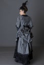 A Victorian woman wearing a striped silk polonaise and a black skirt and standing against a studio backdrop Royalty Free Stock Photo