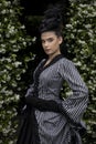 A Victorian woman wearing a striped silk polonaise and a black skirt and standing in a summer garden Royalty Free Stock Photo