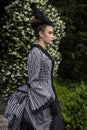 A Victorian woman wearing a striped silk polonaise and a black skirt and standing in a summer garden Royalty Free Stock Photo