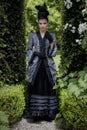 A Victorian woman wearing a striped silk polonaise and a black skirt and standing in a summer garden Royalty Free Stock Photo