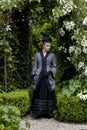 A Victorian woman wearing a striped silk polonaise and a black skirt and standing in a summer garden Royalty Free Stock Photo