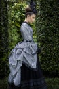 A Victorian woman wearing a striped silk polonaise and a black skirt and standing in a summer garden Royalty Free Stock Photo