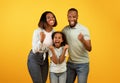 Victory concept. Emotional overjoyed black family shaking fists, gesturing yes and shouting over yellow background