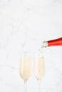 Victory and congratulations background - flow of pouring fizz champagne from red neck bottle to two glasses on  light white marble Royalty Free Stock Photo