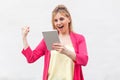 Victory! Portrait of beautiful unbelievable young woman in pink blouse standing and watching and using her tablet with suprised